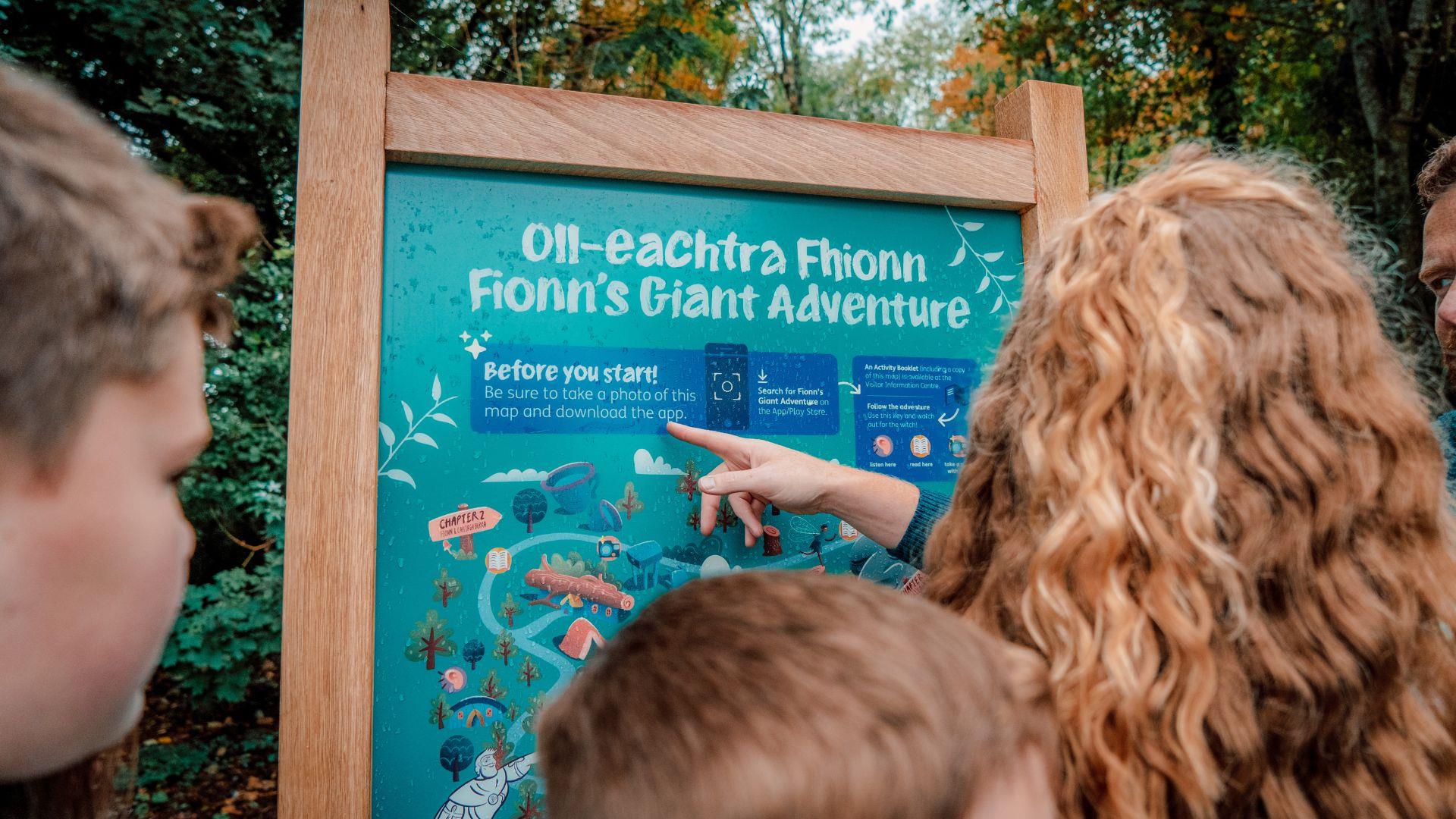 A family reading a sign at the entrance to Fionn's Giant Adventure  at Slieve Gullion Forest Park.