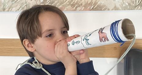 An image of a young boy demonstrating the use of the 'hunting horn' he made during one of the craft workshops.