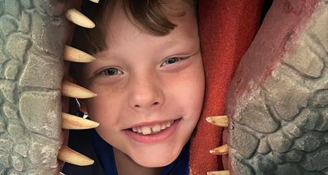 A boy gripped in the mouth of a dinosaur (dino not real)
