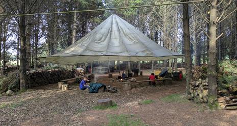 Men at Tepee in forest setting with campfire.