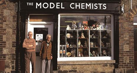 Two gentlemen standing outside 'The Model Chemist' building as part of the Bessbrook Historic Model Village