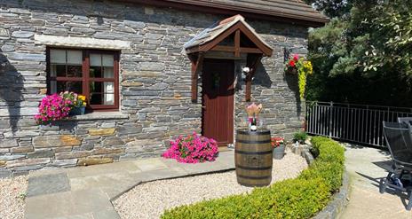 Front garden with paved path leading to the cottage's front door, decorated with flowers and a barrel.