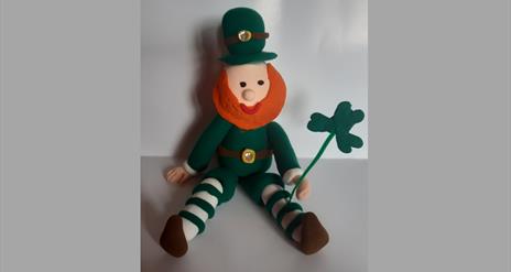 A handmade leprechaun with a shamrock in their hand, sitting on a table, on St Patrick's Day at Newry and Mourne Museum.