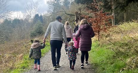 A family enjoying a walk in Slieve Gullion Forest Park. Two adults and two children holding hands, walking up a path together.