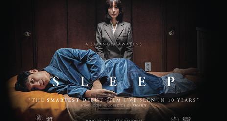 A man lies in a sleeping position, looking forward in horror, while woman stands over him looking directly at the camera.