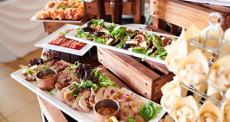 Buffet table with white plates on different tiers. Each has a colourful selection of food, pates, fresh figs, meats and charcuterie.