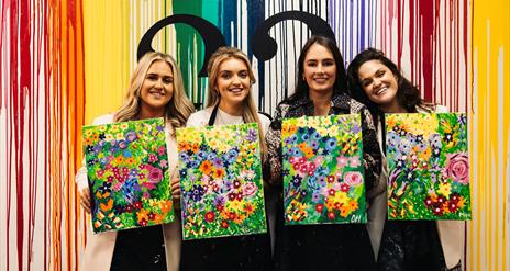 Image of group of girls holding paintings of flowers, painted in a class.