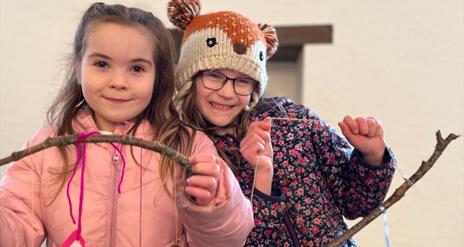 Two girls looking at the camera proudly displaying art they made at the Terrific Trees event.