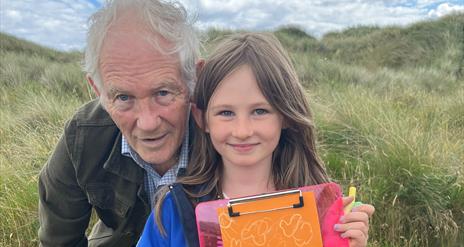 A child and and adult at beach activities at Tyrella Beach. Child holding a clipboard.