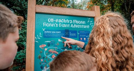 A family reading a sign at the entrance to Fionn's Giant Adventure  at Slieve Gullion Forest Park.