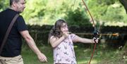 Little girl shooting bow & arrow with father behind her.