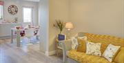 Open plan lounge area with a yellow sofa leading into a kitchen/dining room.