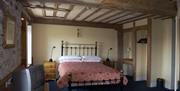 A double bedroom with stone walls and a wooden beam ceiling with a TV, mirror and a window.