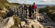 A group of six walkers standing on a bridge and looking out to sea, on the Bloody Bridge Coastal Path.