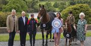 show organisers stand in front of castlewellan lake with a pony and a horse