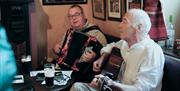 Ceili & Craic in the Mournes. 2 male musicians, a guitar player and accordion performing in bar seated at a table.