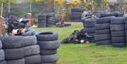 Men in camouflage behind tyres paintballing