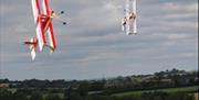 Model aeroplanes flying in the blue sky with green fields behind.