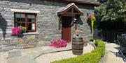 Front garden with paved path leading to the cottage's front door, decorated with flowers and a barrel.