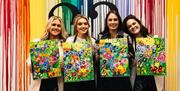 Image of group of girls holding paintings of flowers, painted in a class.