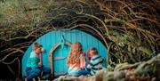 Three children outside a fairy house at Fionn's Giant Adventure at Slieve Gullion Forest Park.