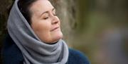 connecting to nature - image of womans head and shoulders with eyes closed. standing with back against a tree.