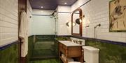 Bathroom with green and white tiles, natural woods and illustrated artwork.