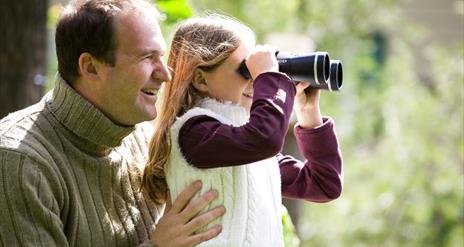 Two people bird watching in Castlewellan Forest Park. The child is looking through binoculars.