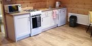 Open plan kitchen, wooden floor, cream wall and floor storage cabinets. Microwave and kettle on work surface with free standing  hob &oven and half fr