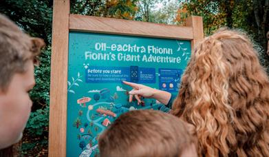 A family reading a sign at the entrance to Fionn's Giant Adventure  at Slieve Gullion Forest Park.