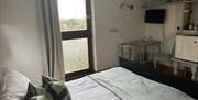 Room with a view interior showing double bed, tv, fridge, small dining area & shelving.