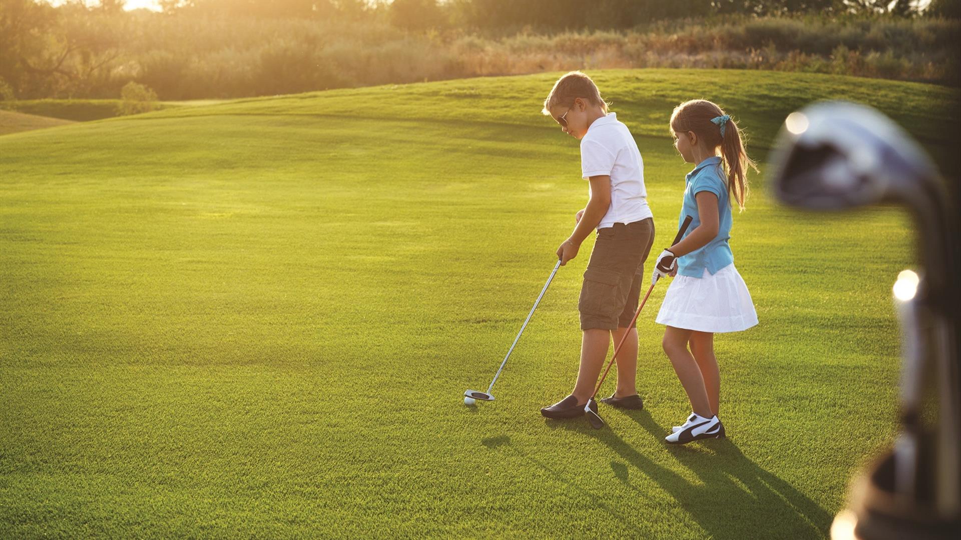 A young boy and girl playing golf on a golf course.