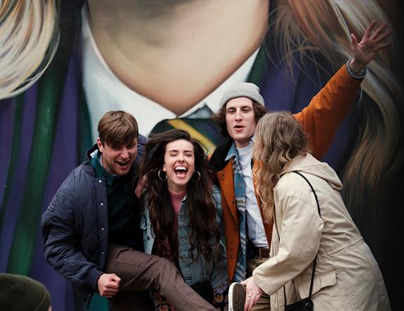 Image shows a group of people having fun in front of the Derry Girls mural