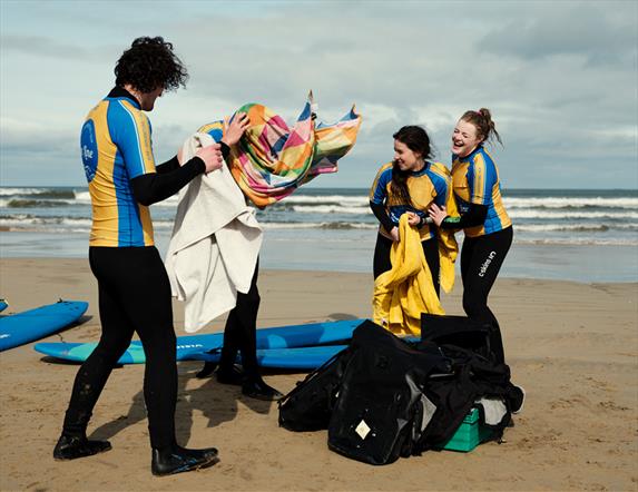 Image shows a group of four surfers on the beach