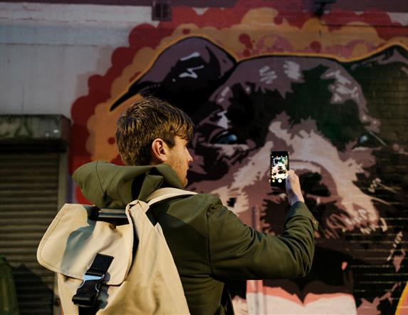 Image shows a man taking a picture on his phone of the Street Art in Belfast