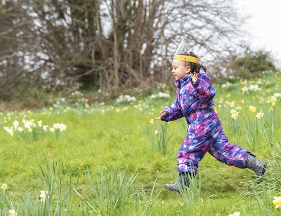 Girl running through meadow wearing easter bunny ears.