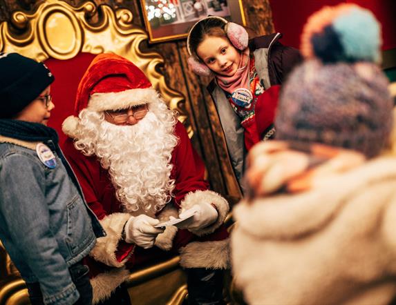 Santa on his chair with a girl and boy on either side reading letters