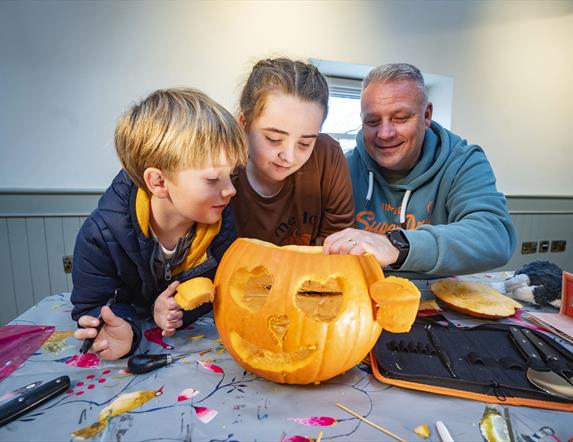 Two children and a man are looking at a pumpkin they have carved together