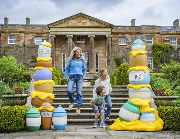 A woman and two children are running down the steps of the South Terrace at Hillsborough Castle. On either side of the steps are brightly coloured sta