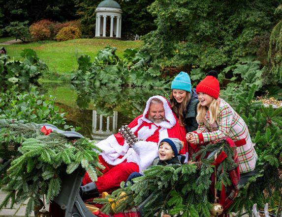 Three children are laughing and sitting with Santa in his sleigh on the grounds of Hillsborough Castle and Gardens. Santa is in a red suit.