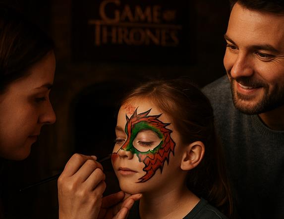 Woman painting a dragon on child's face as father watches.