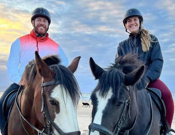 a man and woman sitting on horse back on the beach