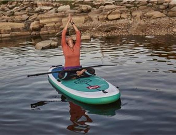 A person sitting in a yoga pose on a SUP board on water