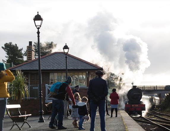 Steam train departing from Whitehead Station with family onlooking from platform