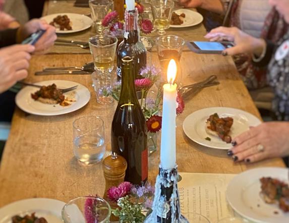 people are eating at a large wooden table by candlelight