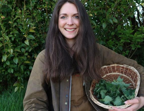 a woman holds a wicker basket containing foraged plants