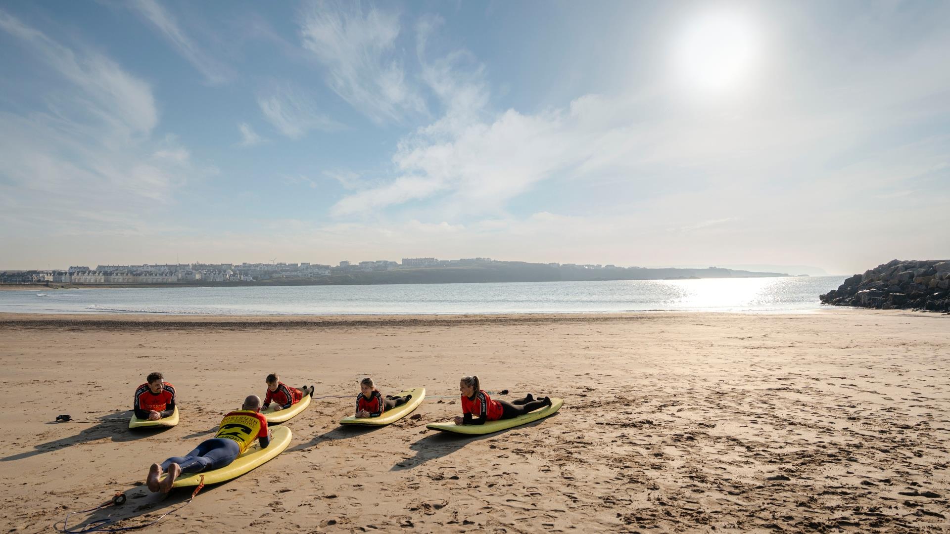 Kids lying on their surfboards on the the sand during a lesson with Portrush Surf School, County Antrim