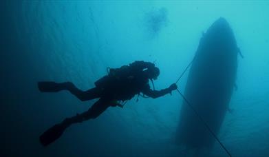 Diver underwater following an anchor line from a boat