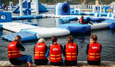 Image shows children wearing life jackets, sitting on the edge of the lake