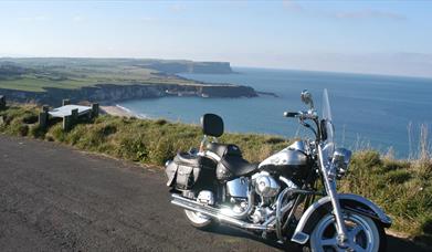 A Harley-Davidson on a road overlooking cliffs with a beach.